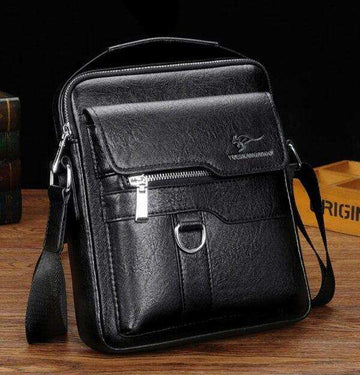 Black leather crossbody laptop bag with zipper pockets on wooden table