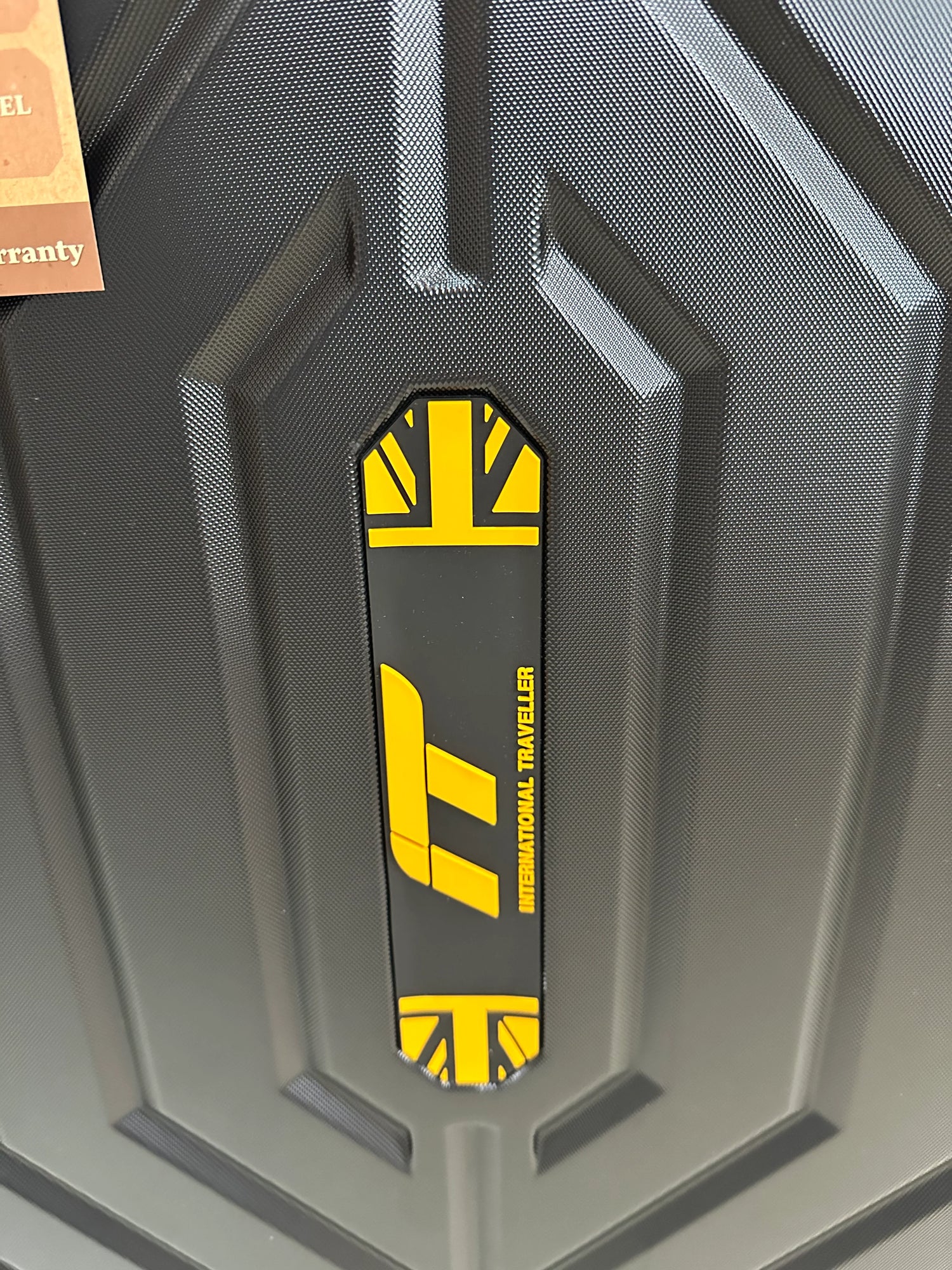 Black hardshell suitcase with yellow International Traveller logo, textured surface design