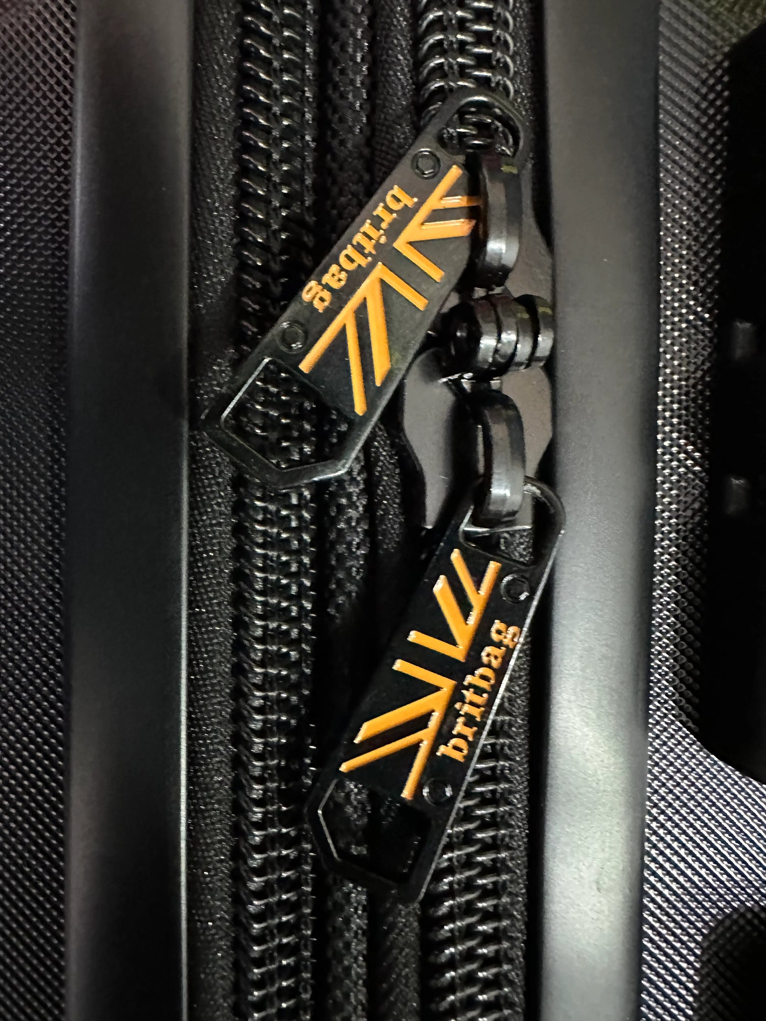 Britbag zipper pull on black luggage with orange logo detail
