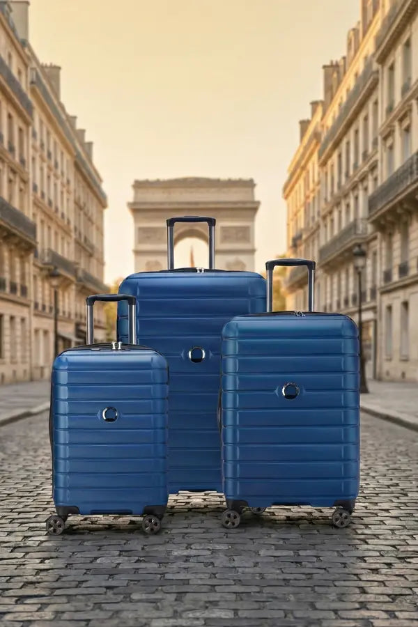 Three blue suitcases of different sizes on a cobblestone street with classical architecture in the background.