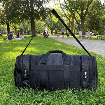 Black duffel bag on grass with people and trees in the background