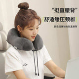 Woman using a grey travel neck pillow while working at a desk, ergonomic cushion for comfort