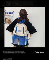Blue and cream student backpack with front pockets and plush charm, worn by person with cap and headphones
