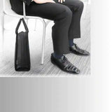 Black leather laptop bag beside business person in black suit and dress shoes