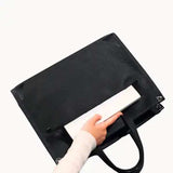Hand placing a laptop into a black tote laptop bag with front pocket on white background